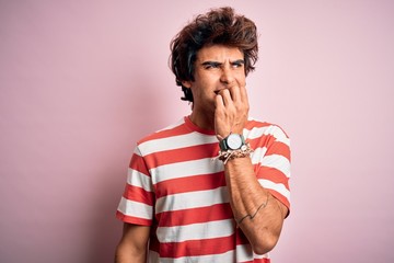 Young handsome man wearing striped casual t-shirt standing over isolated pink background looking stressed and nervous with hands on mouth biting nails. Anxiety problem.