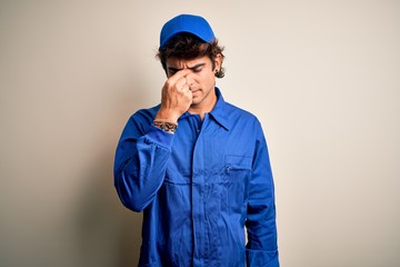 Young mechanic man wearing blue cap and uniform standing over isolated white background tired rubbing nose and eyes feeling fatigue and headache. Stress and frustration concept.
