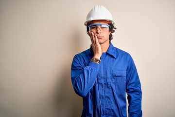 Young constructor man wearing uniform and security helmet over isolated white background thinking looking tired and bored with depression problems with crossed arms.
