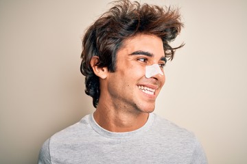 Young handsome man using nose strip standing over isolated white background looking away to side with smile on face, natural expression. Laughing confident.