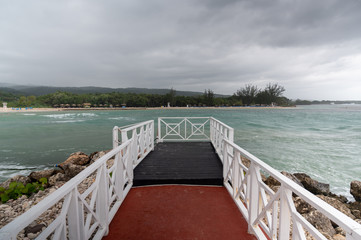 an empty pier sits on the coast line across from a tropical green island on a stormy, overcast day