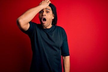 Young handsome african american afro man with dreadlocks wearing casual t-shirt surprised with hand...