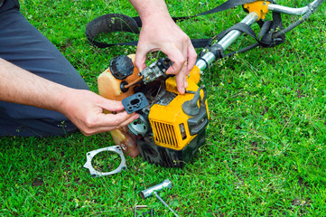 Worker repairs a carburetor in a trimmer or lawn mower that lies on the grass - obrazy, fototapety, plakaty