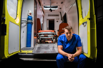 Serious man in a medical iniform sitting in the back of an ambulance car