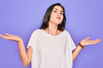 Young beautiful brunette woman wearing casual white t-shirt over purple background clueless and...