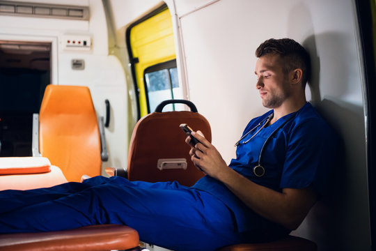 Male paramedic in a blue uniform resting and chatting with someone over the phone
