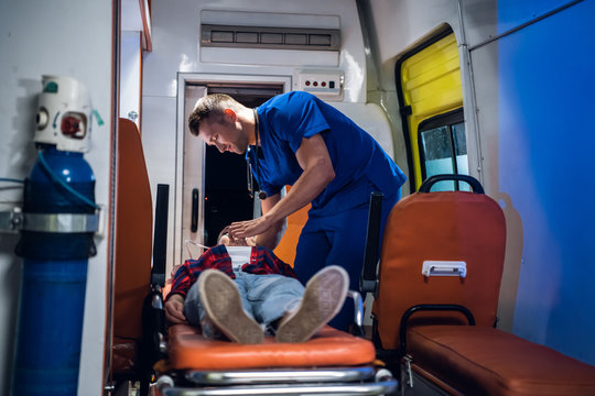A young paramedic in a uniform gives an oxygen mask to his patient