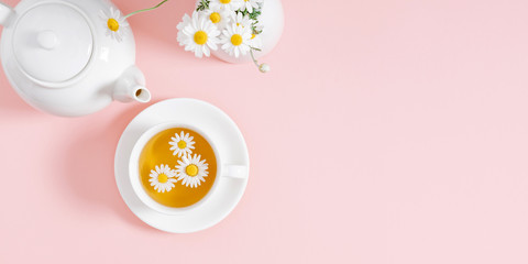 White chamomiles, cup and teapot on pastel pink background. Herbal tea of chamomile flower. Chamomile tea concept. Flat lay, top view, copy space