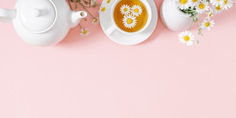 Fototapeta na wymiar White chamomiles, cup and teapot on pastel pink background. Herbal tea of chamomile flower. Chamomile tea concept. Flat lay, top view, copy space