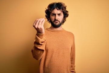 Young handsome man with beard wearing casual sweater standing over yellow background Doing Italian gesture with hand and fingers confident expression