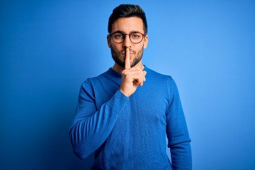 Young handsome man with beard wearing casual sweater and glasses over blue background asking to be...