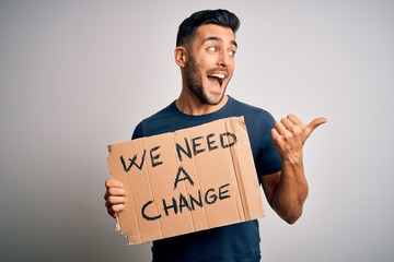 Young handsome activist man protesting for the enviroment hoding cardboard pointing and showing with thumb up to the side with happy face smiling