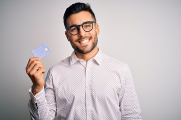 Young business man holding credit card over isolated background with a happy face standing and...