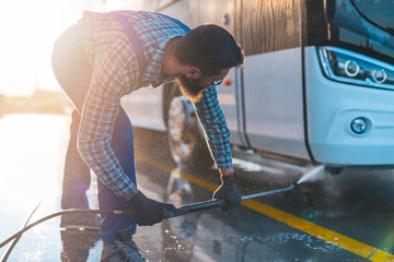 Young man washing bus using high pressure water. Selective focus.
