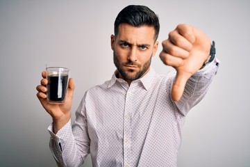 Young handsome man drinking a cup of hot coffee over white isolated background with angry face, negative sign showing dislike with thumbs down, rejection concept