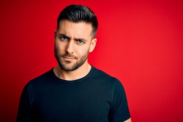 Obraz premium Young handsome man wearing casual black t-shirt standing over isolated red background skeptic and nervous, frowning upset because of problem. Negative person.