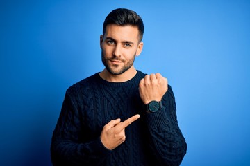 Young handsome man wearing casual sweater standing over isolated blue background In hurry pointing...