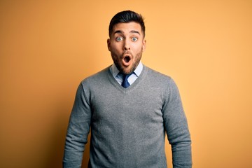 Fototapeta premium Young handsome businessman wearing elegant sweater and tie over yellow background afraid and shocked with surprise expression, fear and excited face.