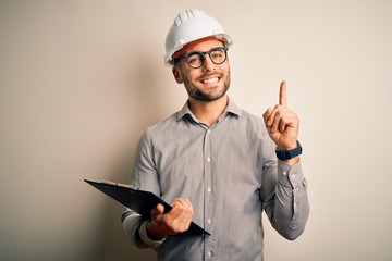 Young architect inspector man wearing builder safety helmet and using clipboard surprised with an...