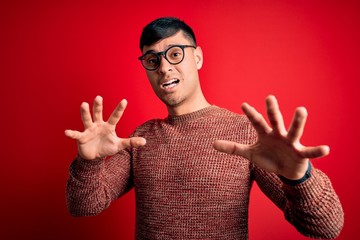 Young handsome hispanic man wearing nerd glasses over red background afraid and terrified with fear...