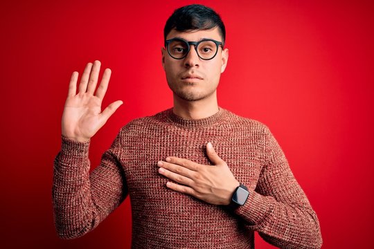 Young handsome hispanic man wearing nerd glasses over red background Swearing with hand on chest and open palm, making a loyalty promise oath