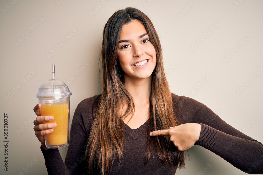 Poster young beautiful girl drinking glass of healthy orange juice over isolated white background with surp