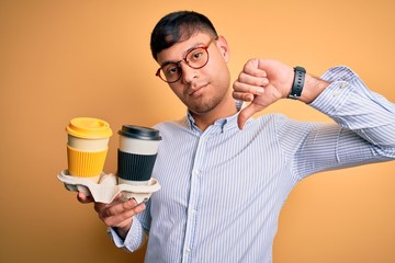 Young scholarship holder business man holding take away coffee over isolated yellow background with...