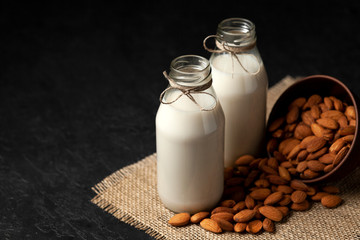 almond milk in bottles with nuts on a black table, a variety of dairy products without sugar and lactose, a vegetarian drink