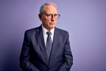 Grey haired senior business man wearing glasses and elegant suit and tie over purple background skeptic and nervous, frowning upset because of problem. Negative person.