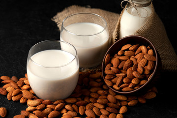 almond milk without sugar and lactose in glass with sprinkled nuts, vegetarian milk drink on a dark black table