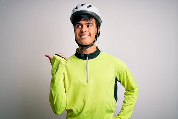 Young handsome cyclist man wearing security bike helmet over isolated white background smiling with happy face looking and pointing to the side with thumb up.