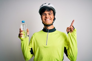 Young handsome cyclist man wearing security bike helmet drinking bottle of water surprised with an idea or question pointing finger with happy face, number one