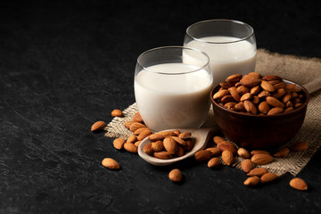 almond milk in a glass with nuts on a dark background, a healthy dairy product without lactose on a black table