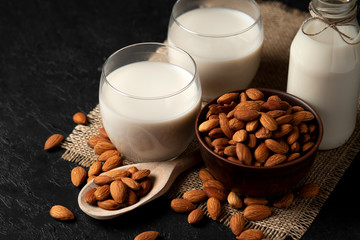 glass of almond milk without lactose and sugar with sprinkled nuts on a dark background, a veggie milk drink on a black table
