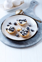 Little mascarpone tart with fresh bilberries on bright wooden background.	