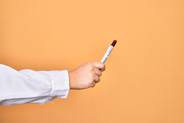 Hand of caucasian young woman holding tests tube with coronavirus results over isolated yellow background