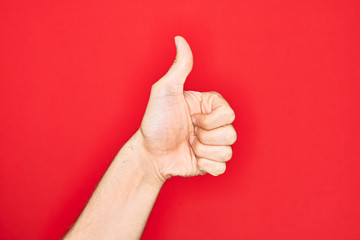 Hand of caucasian young man showing fingers over isolated red background doing successful approval gesture with thumbs up, validation and positive symbol