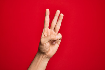 Hand of caucasian young man showing fingers over isolated red background counting number 3 showing three fingers
