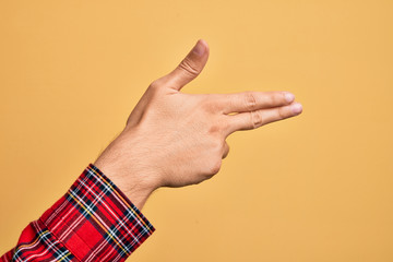 Hand of caucasian young man showing fingers over isolated yellow background gesturing fire gun weapon with fingers, aiming shoot symbol