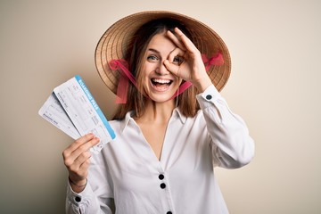 Young beautiful redhead tourist woman wearing asian traditional hat holding boarding pass with happy face smiling doing ok sign with hand on eye looking through fingers