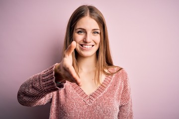 Fototapeta premium Young beautiful redhead woman wearing casual sweater over isolated pink background smiling friendly offering handshake as greeting and welcoming. Successful business.