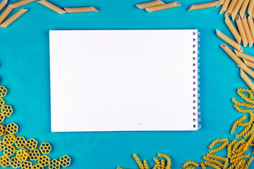 different varieties of macaroni with a notebook on a blue background.