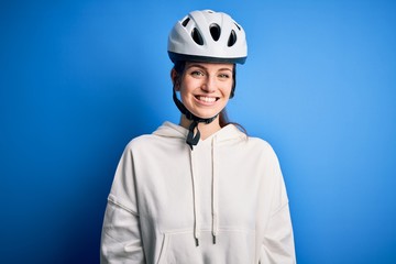 Young beautiful redhead cyclist woman wearing bike helmet over isolated blue background with a happy and cool smile on face. Lucky person.