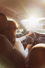 Young beautiful woman driving a car on road in the sunlight.