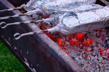  Juicy and fresh slices of pork are strung on metal skewers, wrapped in aluminum foil and grilled on charcoal. Fragrant smoke. Appetizing delicacy of natural meat in the open air on a spring day.