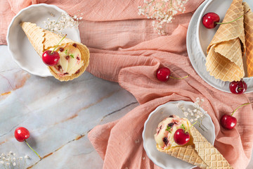 Traditional waffle cones with ice cream and cherry fruits on marble stone surface
