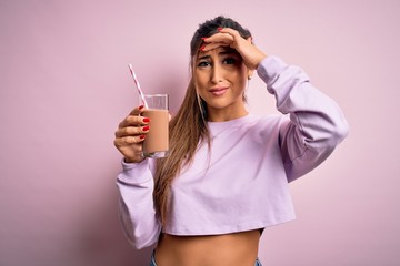Young beautiful fitness woman drinking protein chocolate milkshake before gym stressed with hand on head, shocked with shame and surprise face, angry and frustrated. Fear and upset for mistake.