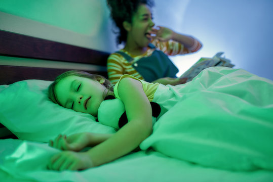 For Kids Comfort. African American Woman Baby Sitter Yawning, Reading Book To Cute Little Girl In The Evening. Nanny Holding Book While Kid Listening To Fairy Tale, Falling Asleep