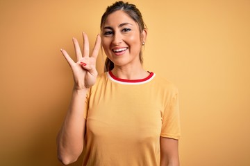 Young beautiful athletic woman wearing casual t-shirt and ponytail over yellow background showing and pointing up with fingers number four while smiling confident and happy.