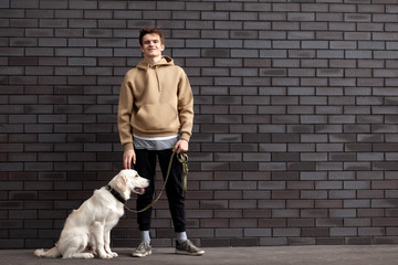young guy with a puppy of a retriever stands on the street against the background of the wall and smiles